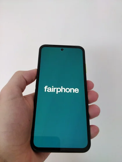 Une main qui tien un fairphone, l’écran affiche la marque en blanc sur fond vert