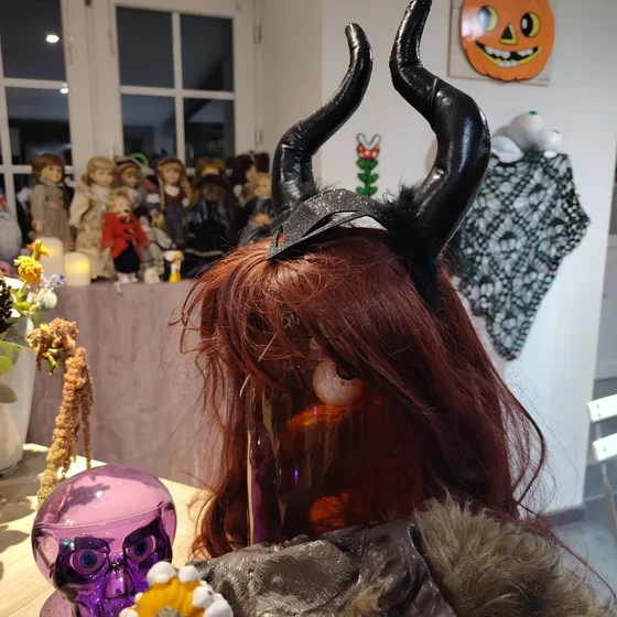 Photo d’un bocal contenant des yeux sur lequel a été posé une perruque et les cornes de Maléfique.
Autour, plein de décorations d’Halloween, donc une collection de poupées malaisante au bord d’une fenêtre.