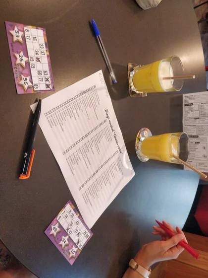 Une table avec 2 grilles de loto, et une liste de nom de moceau de musique des années 2000 associé a chaque numéro.
Il y a également deux verres d’orangina.
