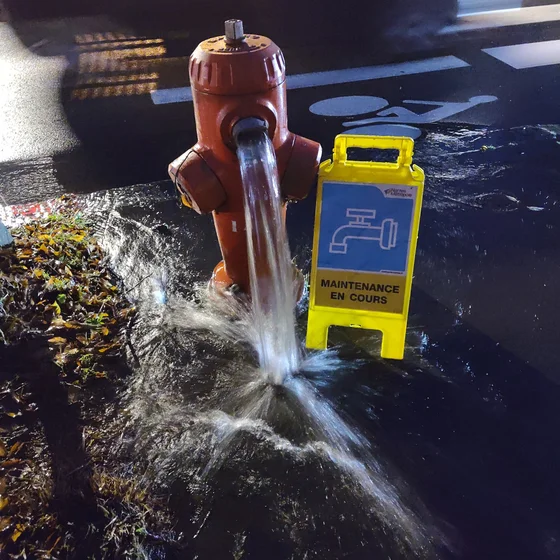 Photo d’un borne à incendie ouverte dans le vide à coté d’un panneau « maintenance en cours »