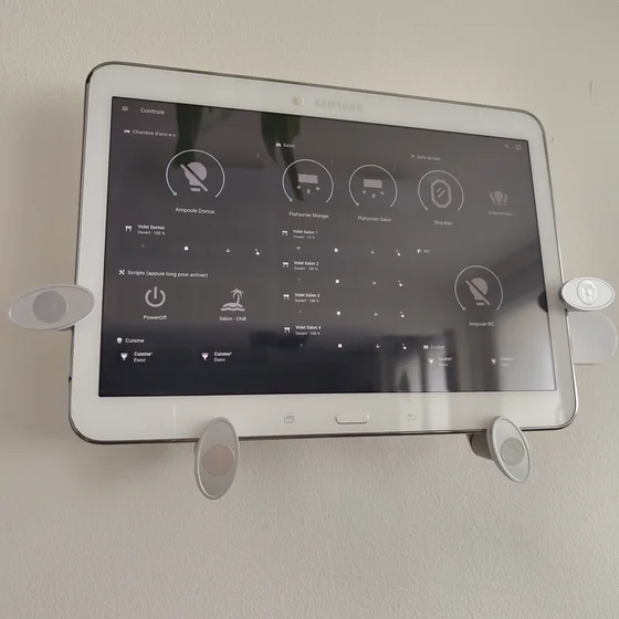 Une tablette samsung fixée au mur, elle affiche une interface Home Assistant avec 3 collones d’intérupteurs.